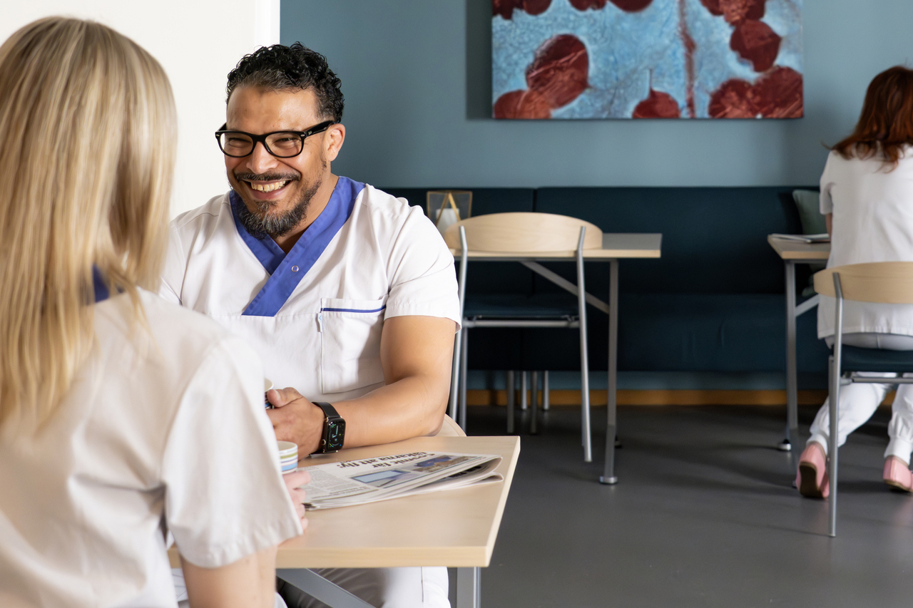 Pausutrymme i kontorsmoduler från Expandia vid Centralsjukhuset Karlstad. Två personer i vårdkläder sitter vid ett bord och samtalar över kaffe i en ljus och lugn miljö, med fler sittplatser och kollegor i bakgrunden.