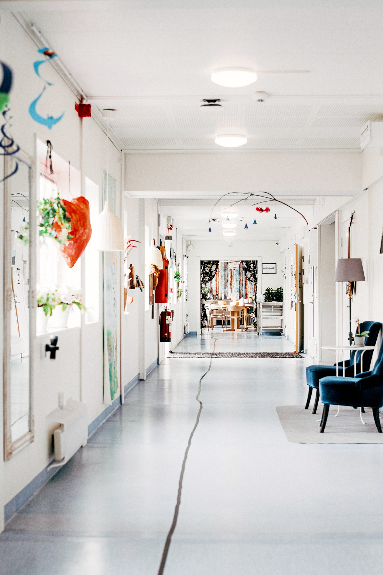 Ljus och inbjudande korridor med konst på väggarna, sittplatser längs sidan och dekorationer i taket. I bakgrunden syns ett gemensamt utrymme med bord och stolar.