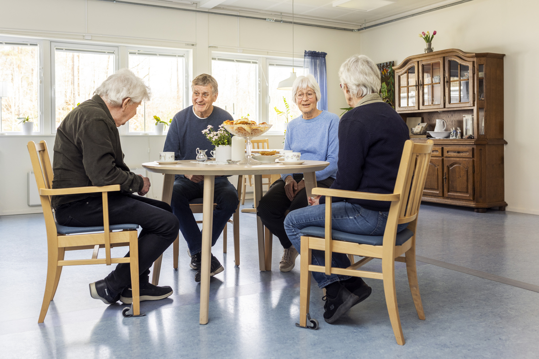 Fyra boende sitter runt ett bord och fikar tillsammans vid Borggården demensvård i Olofström. Rummet är ljust och möblerat för gemenskap och samvaro i en modullösning från Expandia.